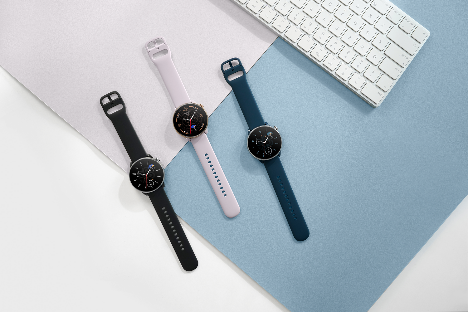 Tres smartwatches en diferentes colores sobre un escritorio, con un teclado al fondo.
