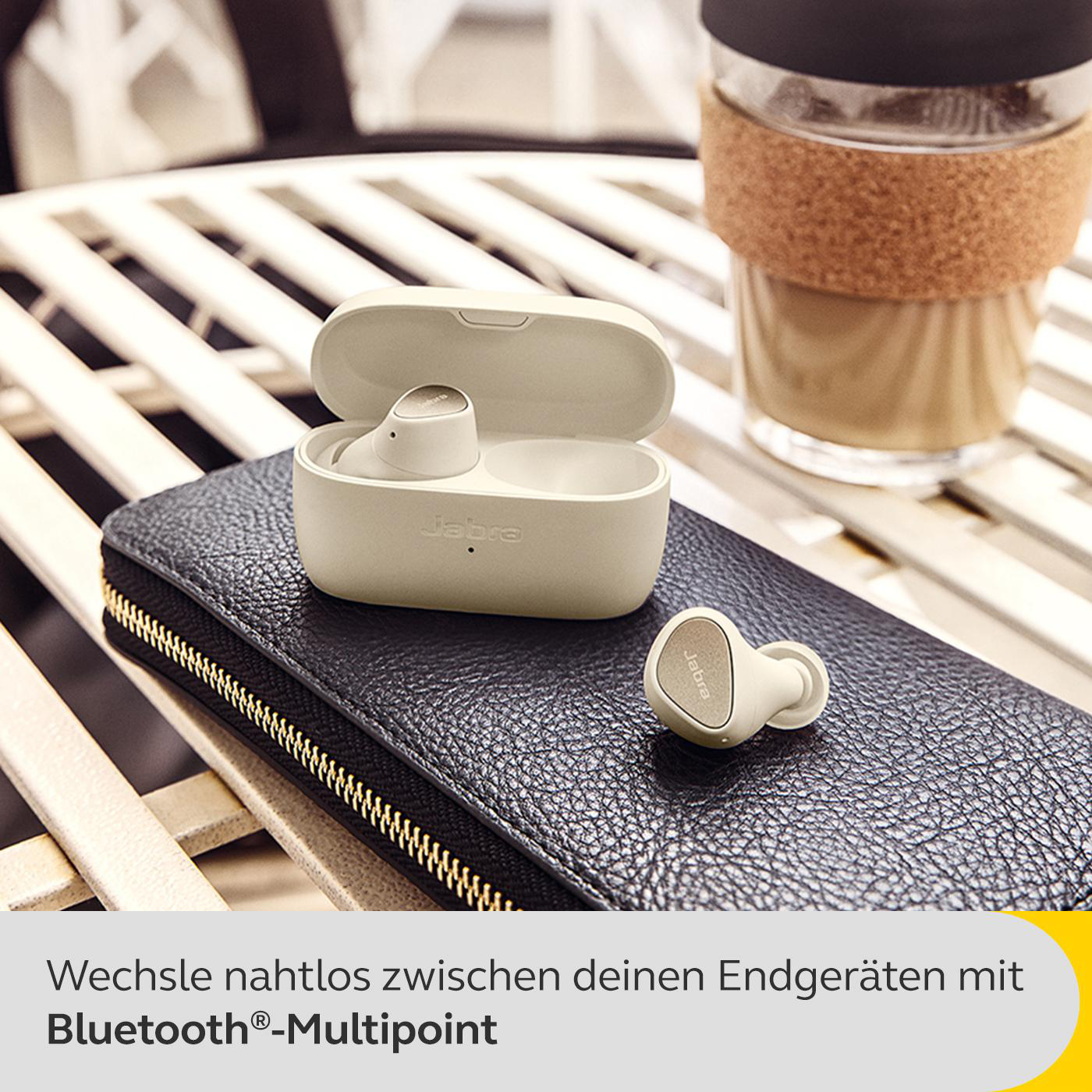 Ohrhörer in einem Ladecase auf einer schwarzen Brieftasche, mit einer Kaffeetasse im Hintergrund.