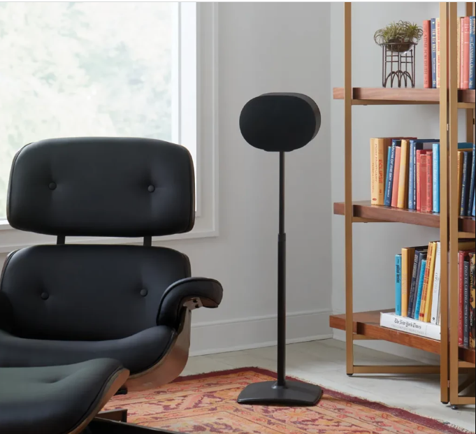 Un fauteuil en cuir noir avec repose-pieds est assis à côté d'une haute enceinte sur un tapis.