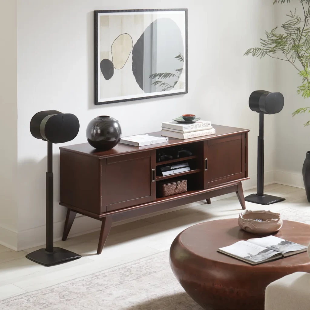 Salon moderne avec console multimédia en bois sombre, haut-parleurs sur pieds et art abstrait.