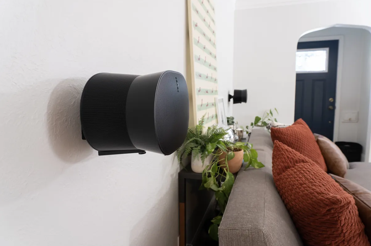 Schwarze Lautsprecher an weißer Wand, daneben ein Sofa mit Kissen und Pflanzen.