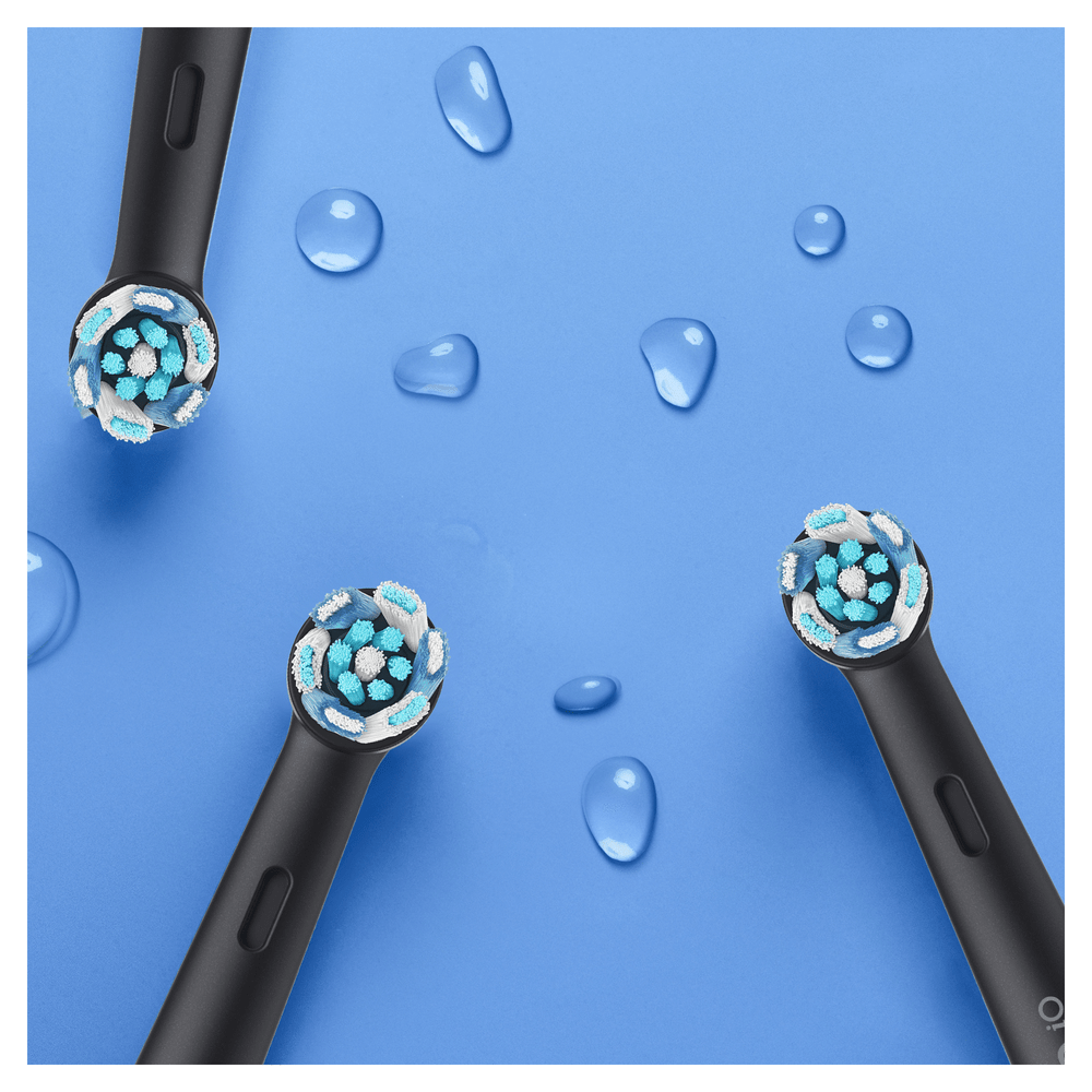 Primer plano de tres cabezales de cepillo de dientes eléctricos negros y gotas de agua sobre una superficie azul.