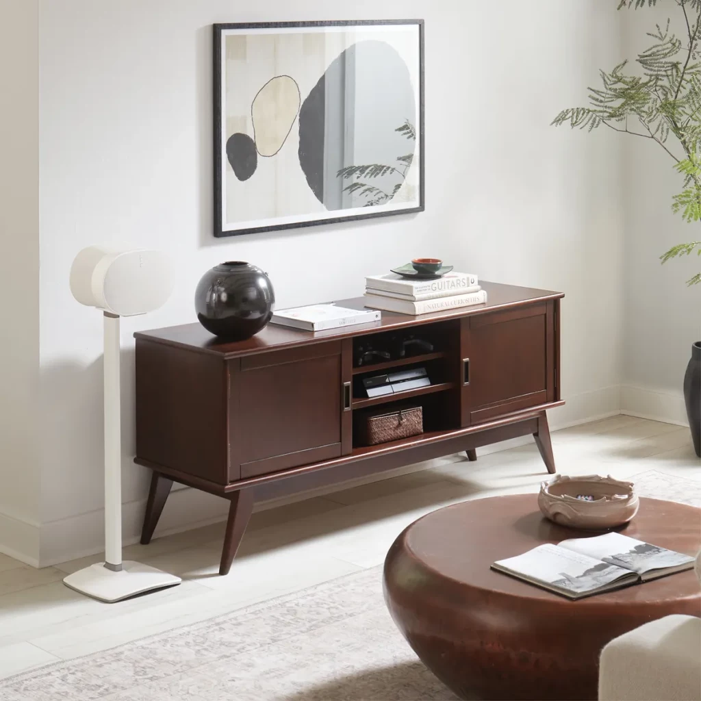 Salon avec un meuble marron, de l'art et un haut-parleur blanc sur pied. Une table basse devant.