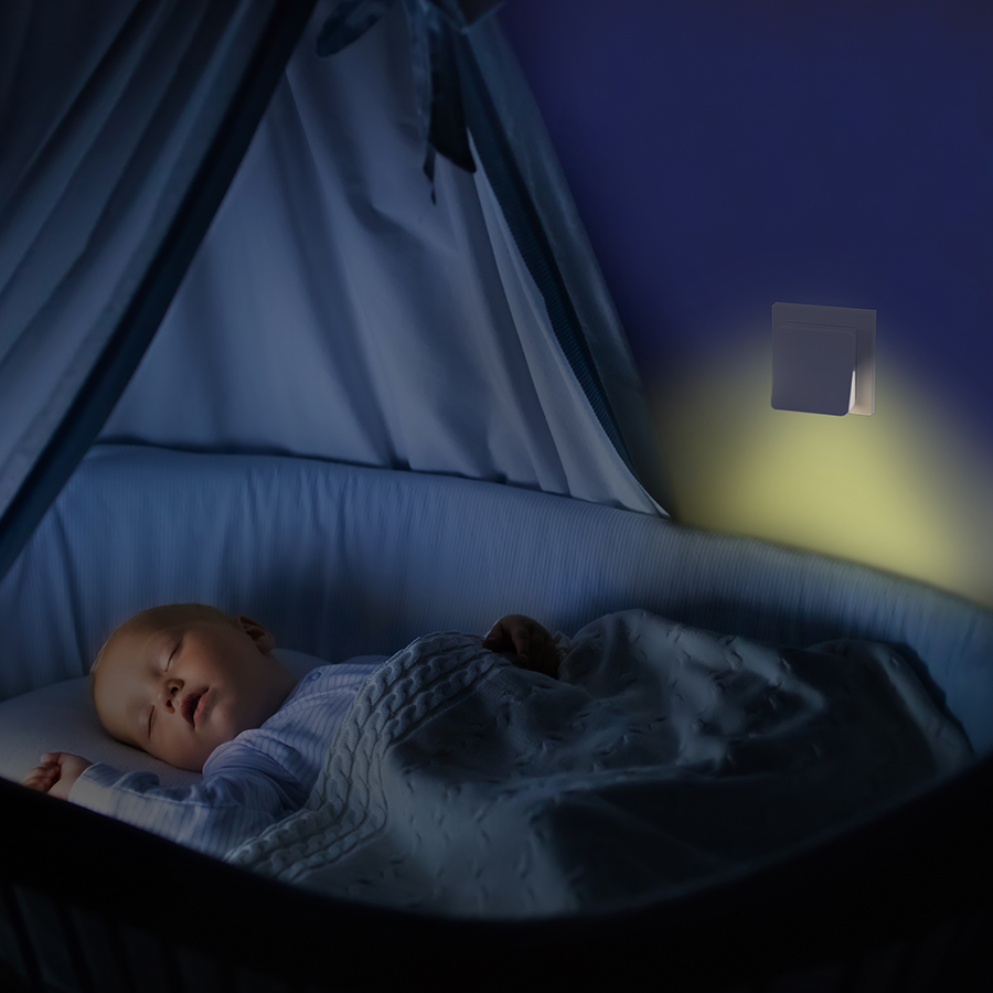 Baby sleeping in a crib at night, with a soft night light on the wall.