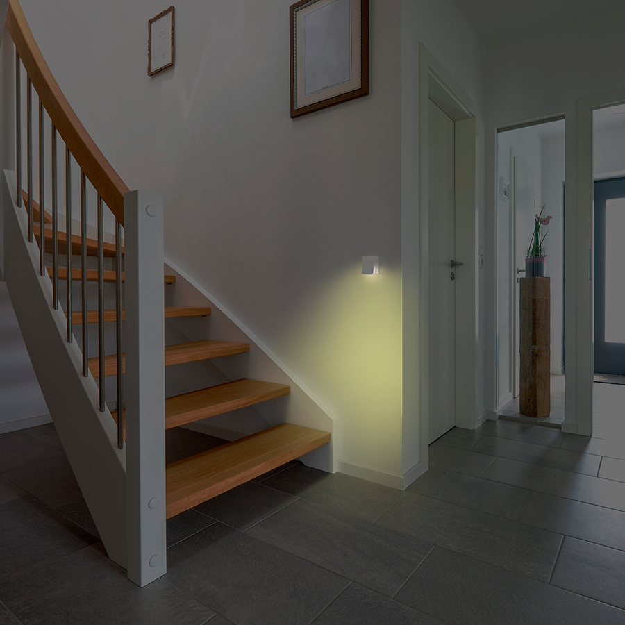 A staircase, illuminated by a wall light. A hallway and a door can be seen in the background.