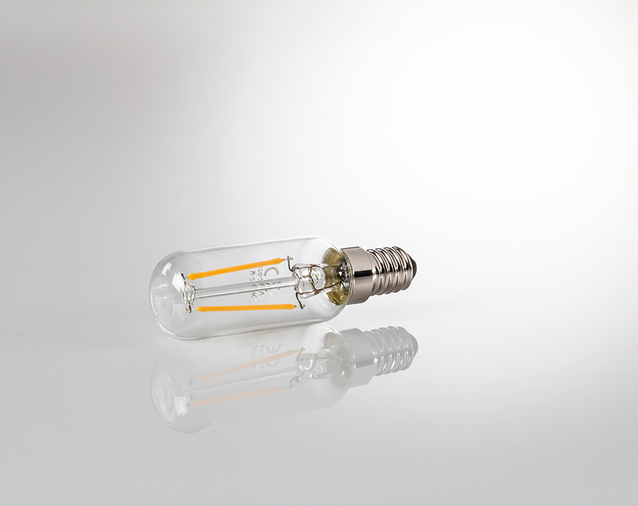 A lightbulb, with two yellow filaments, laying on a reflective surface.