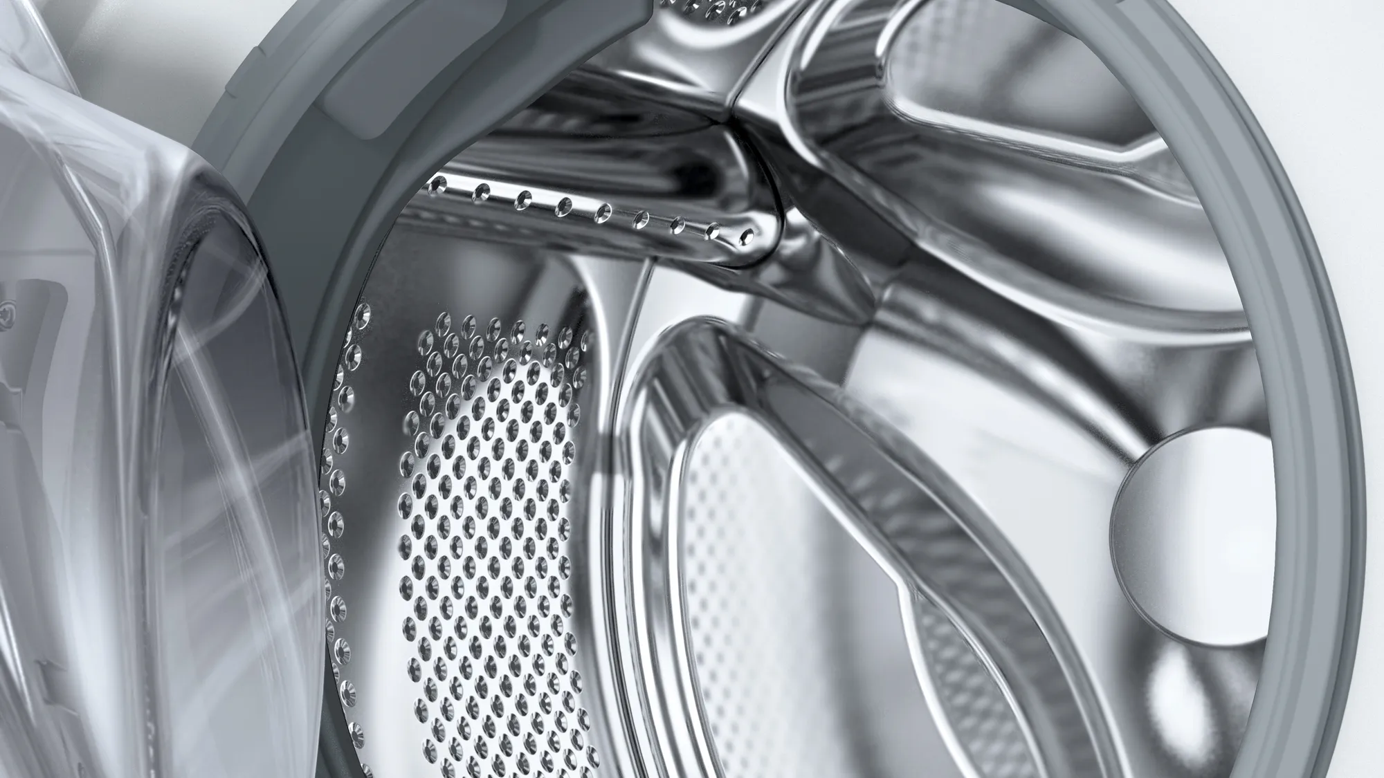 Gros plan sur le tambour d'une machine à laver avec des perforations. Le tambour est métallique, avec une porte en plastique transparente.