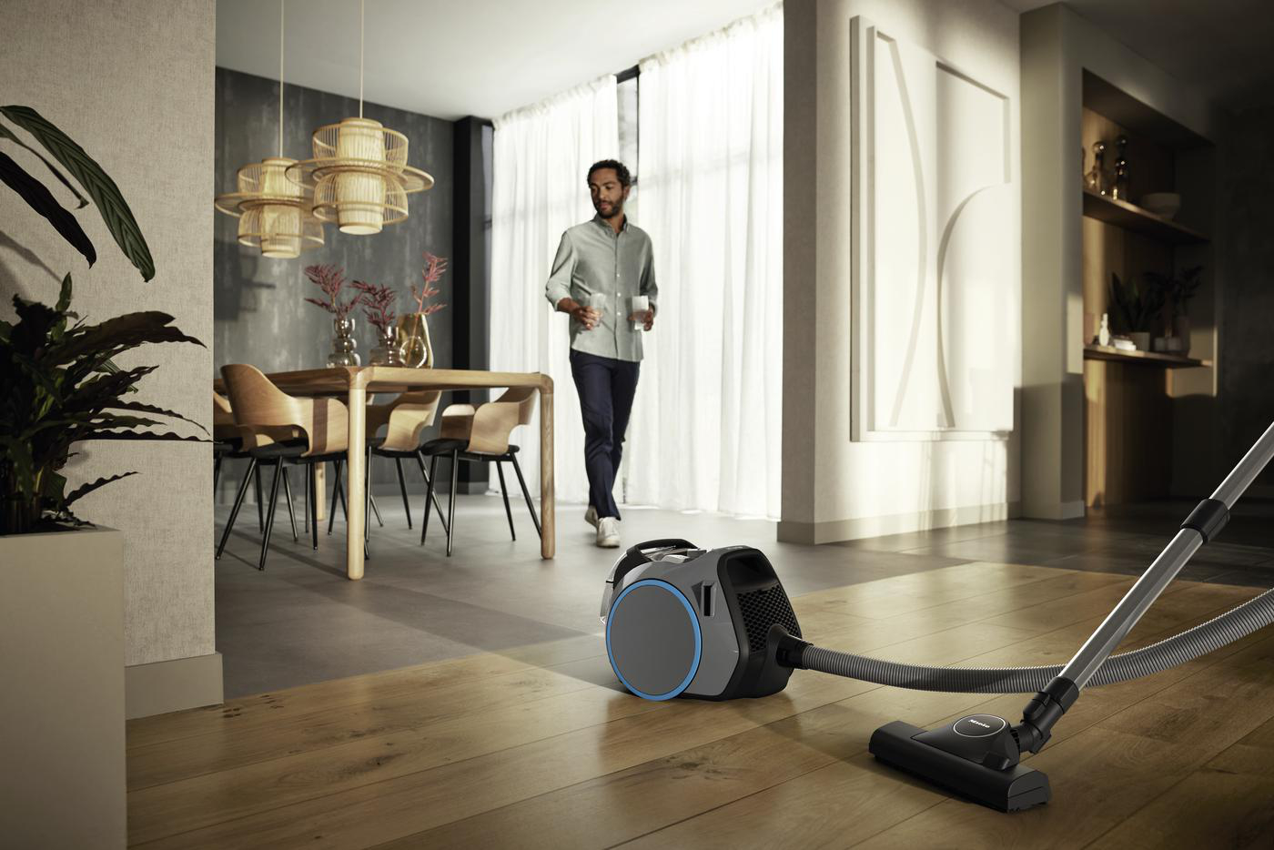 Ein Mann geht in einem modernen Wohnzimmer, ein Staubsauger steht auf dem Boden.