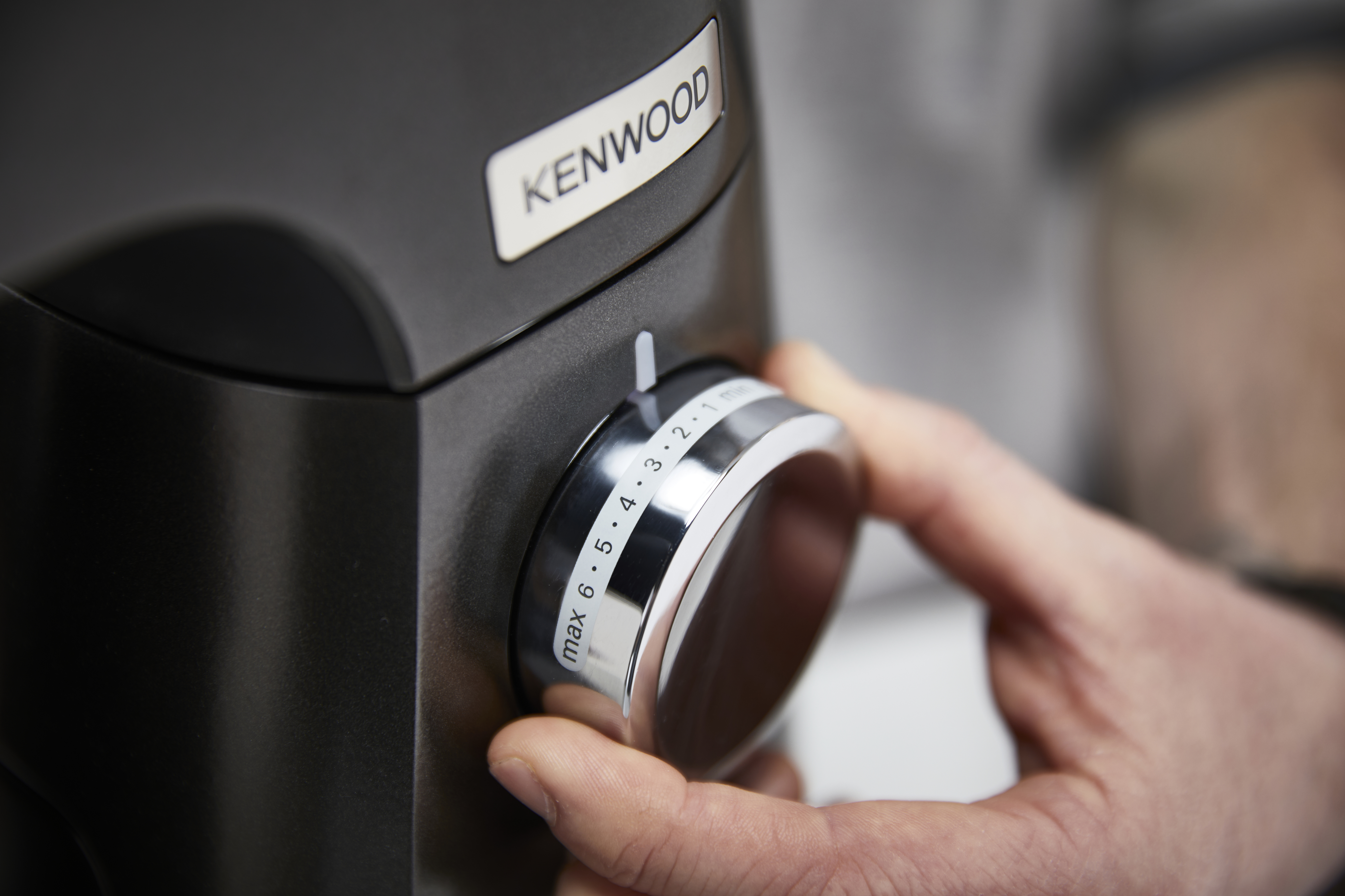 Nahaufnahme einer Hand, die einen Geschwindigkeitsregler an einer Kenwood Küchenmaschine einstellt.