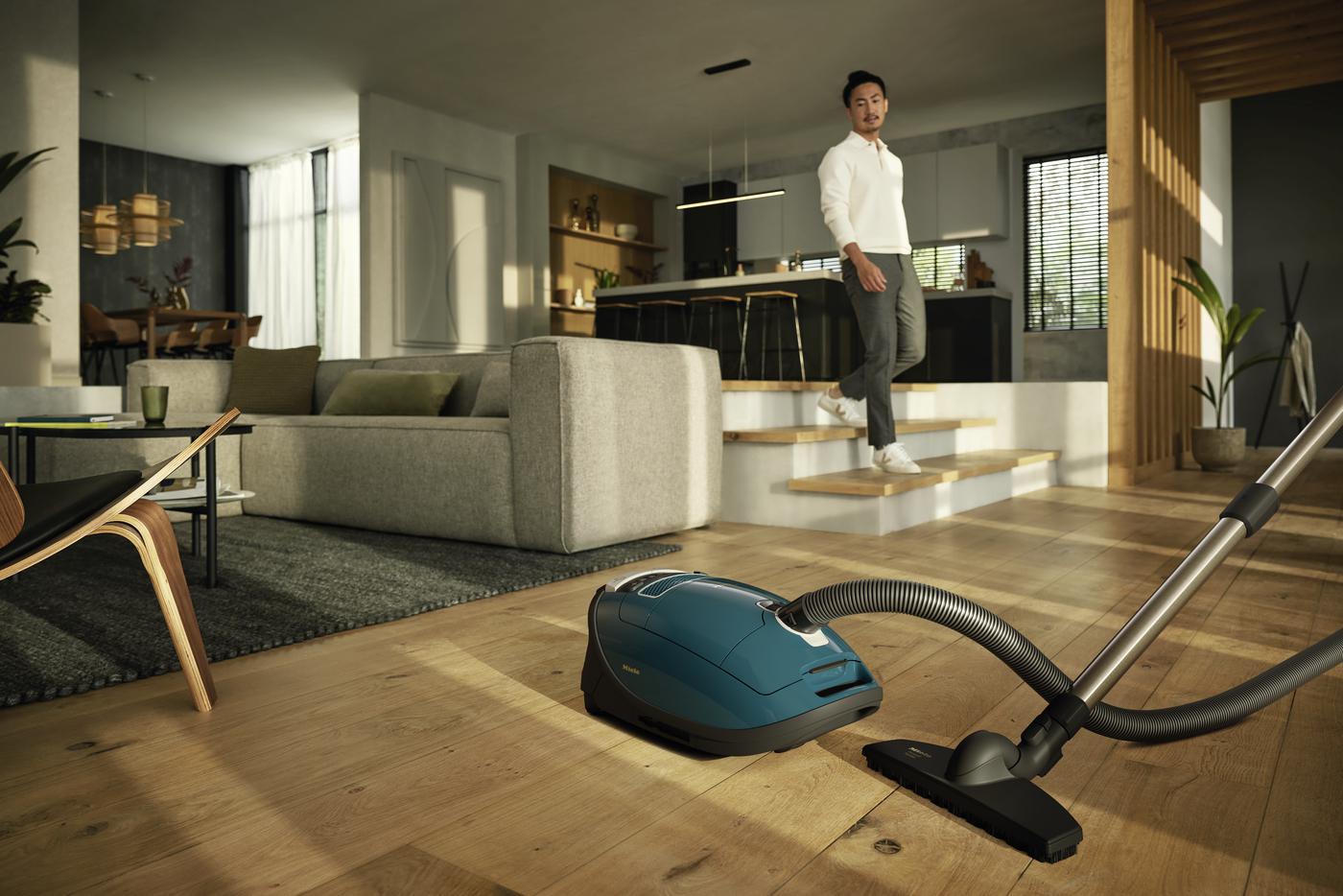 Ein teal Miele Staubsauger auf Holzboden. Im Hintergrund geht ein Mann.