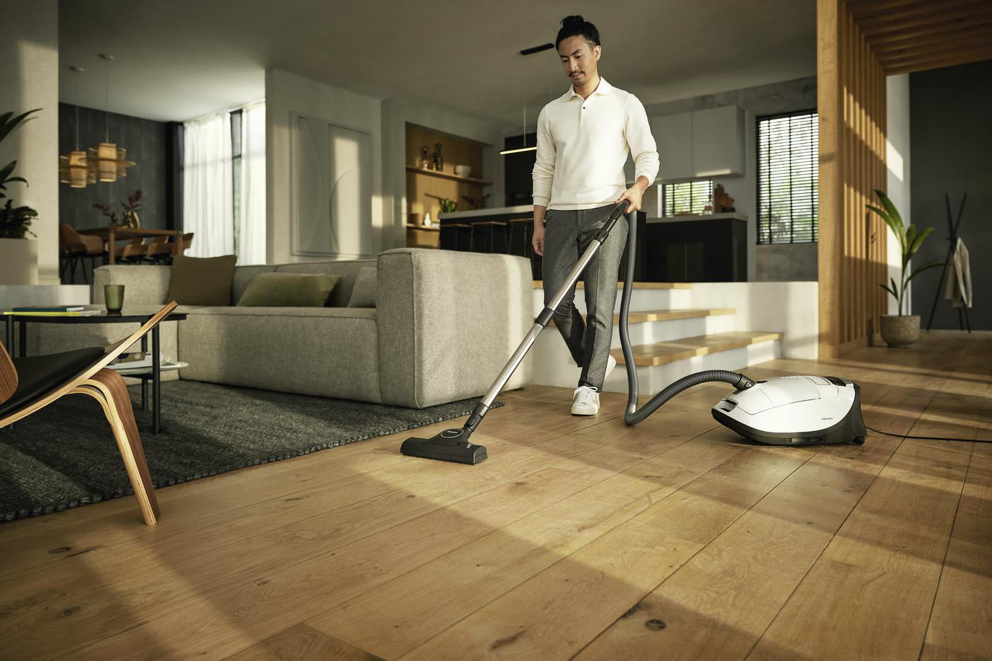 Eine Person, die einen Holzboden in einem modernen Wohnzimmer staubsaugt. Ein weißer Staubsauger ist sichtbar.