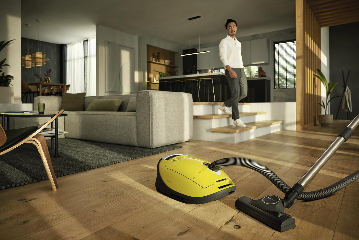Ein Mann geht auf einem Holzboden und saugt mit einem gelben Staubsauger. Modernes Wohnzimmer.