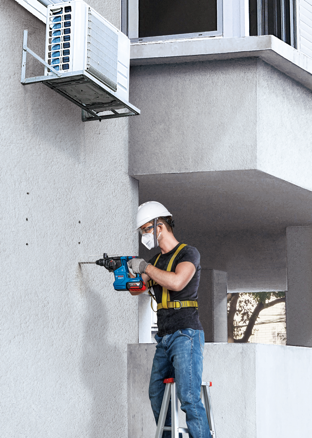 Sisakot viselő férfi falat fúr, felette légkondicionálóval.