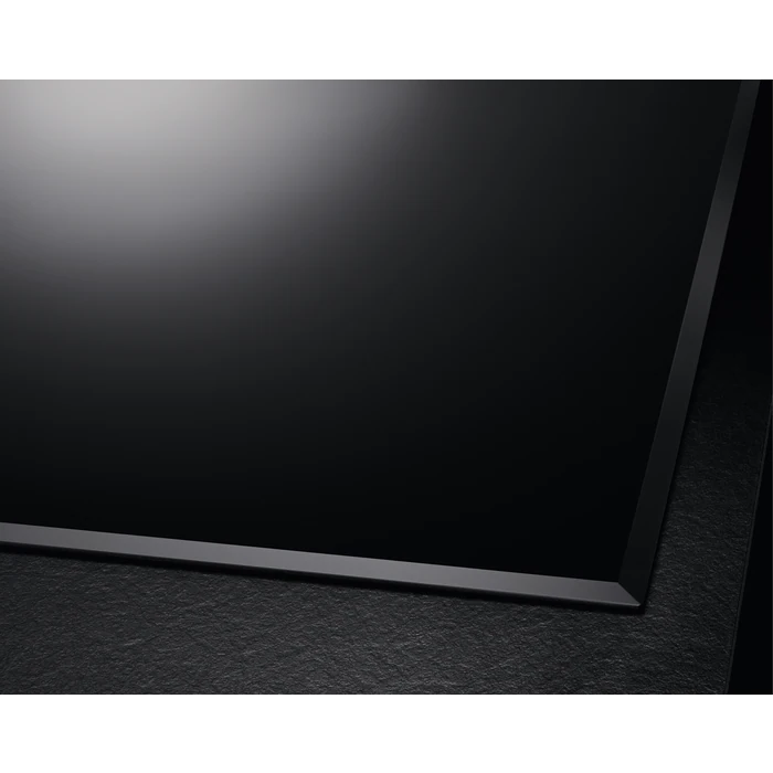Primer plano de una placa de vitrocerámica negra con un borde biselado. La superficie refleja la luz.