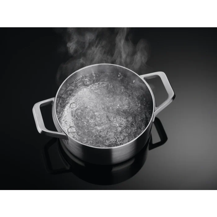 Una olla de acero inoxidable con agua hirviendo, vapor saliendo de la superficie del agua.