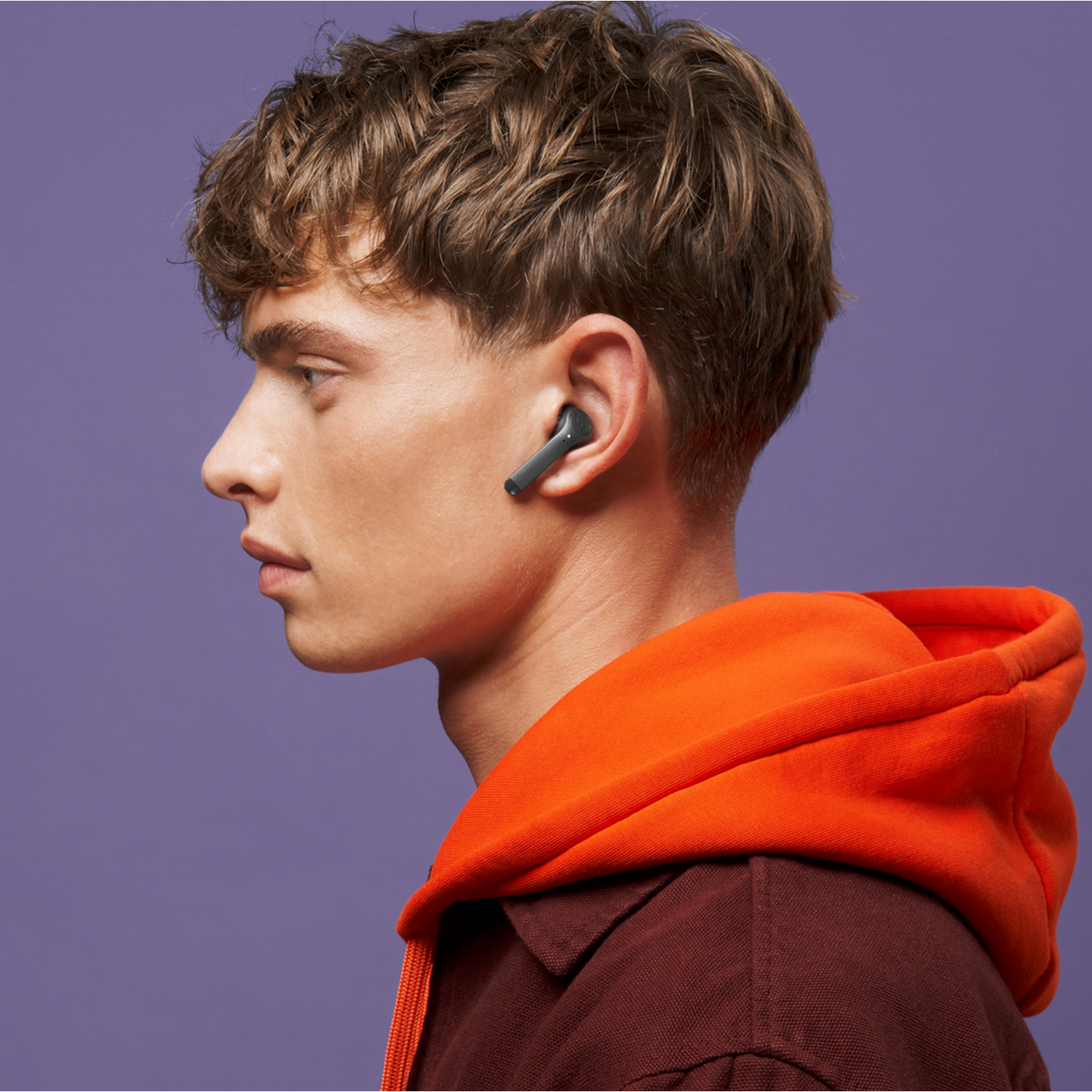 Jonge man met oordopjes, draagt een rode hoodie, paarse achtergrond.