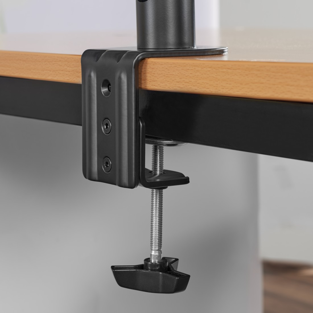 Una abrazadera metálica negra para montar un monitor en un escritorio de madera.