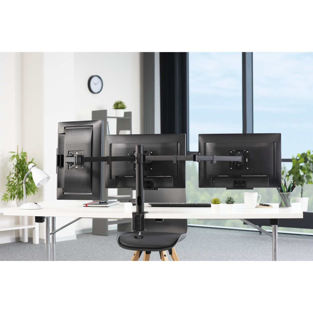 Configuración de oficina con tres monitores, un escritorio blanco y una ventana al fondo.