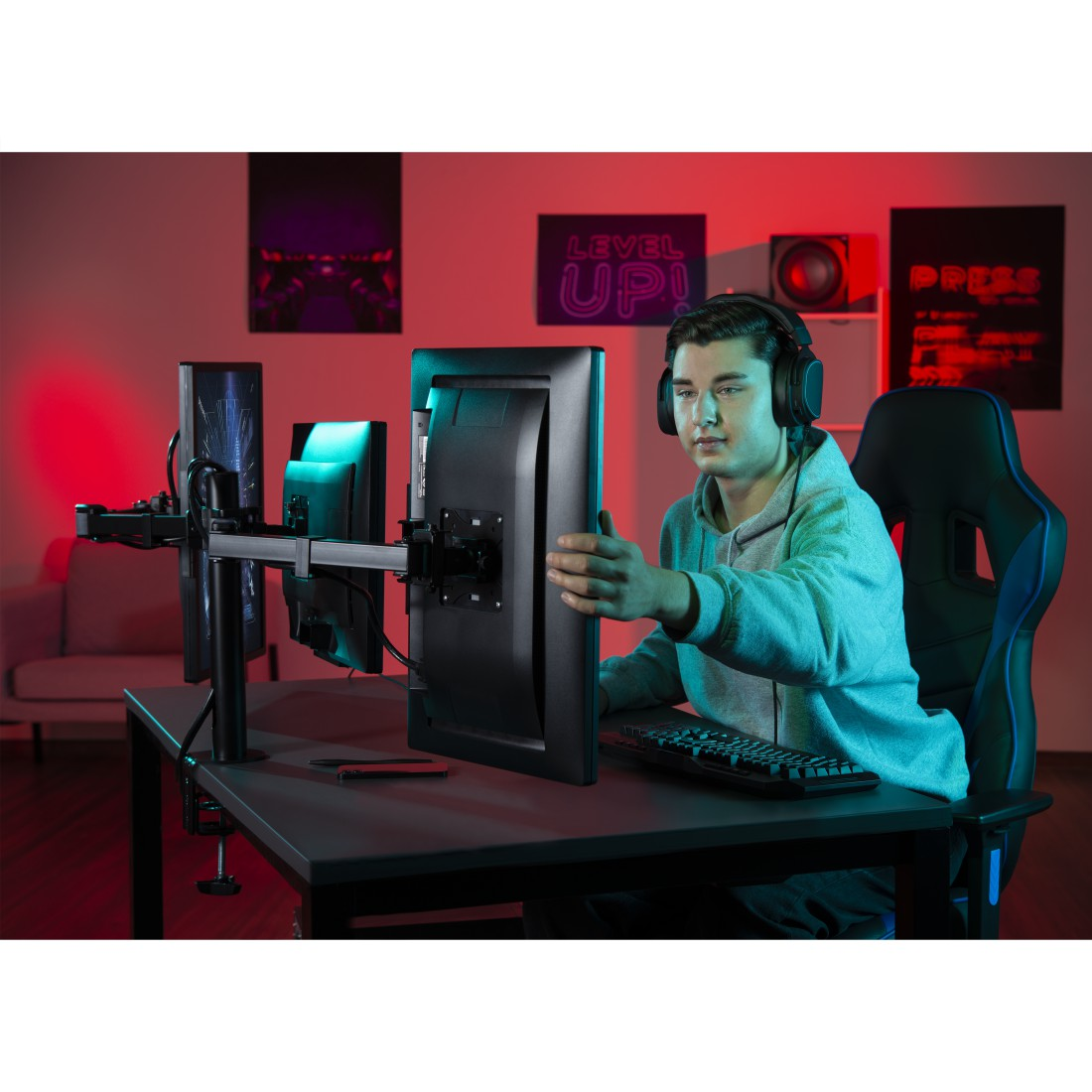 Un jugador ajusta un monitor en un escritorio, usando auriculares. Carteles y luces en el fondo.