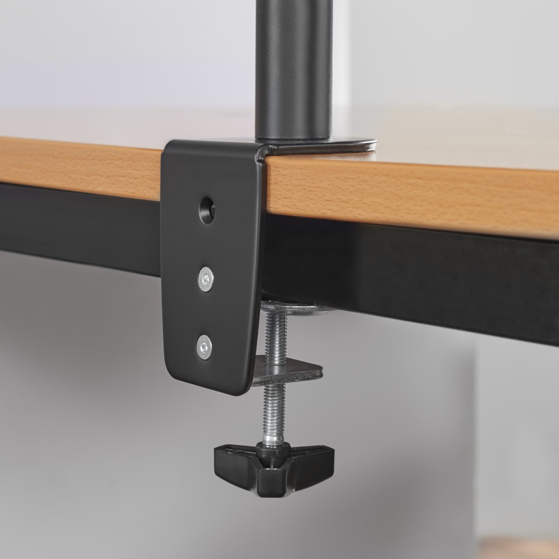 Una abrazadera negra está sujeta a una mesa de madera. La abrazadera es de metal y tiene tornillos.