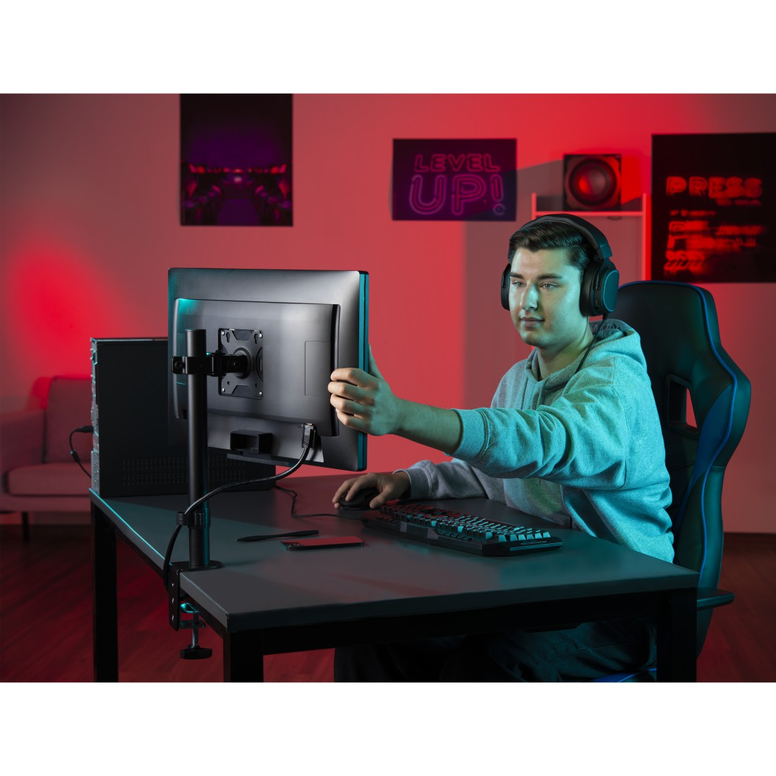 Un jugador en una habitación con monitor y ordenador. Iluminación ambiental roja y carteles.