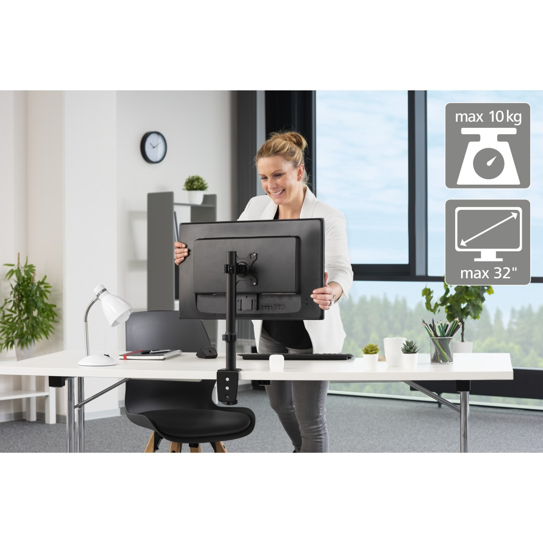 Una mujer instala un monitor en un escritorio blanco, con una lámpara y un reloj.