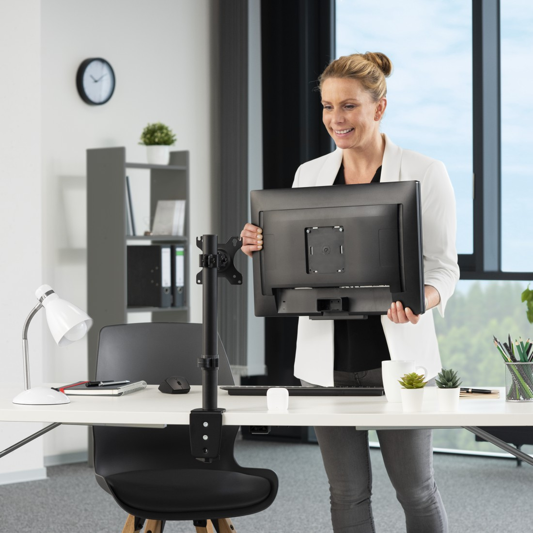 Una mujer sostiene un monitor de computadora, lista para montarlo en un soporte de escritorio negro.
