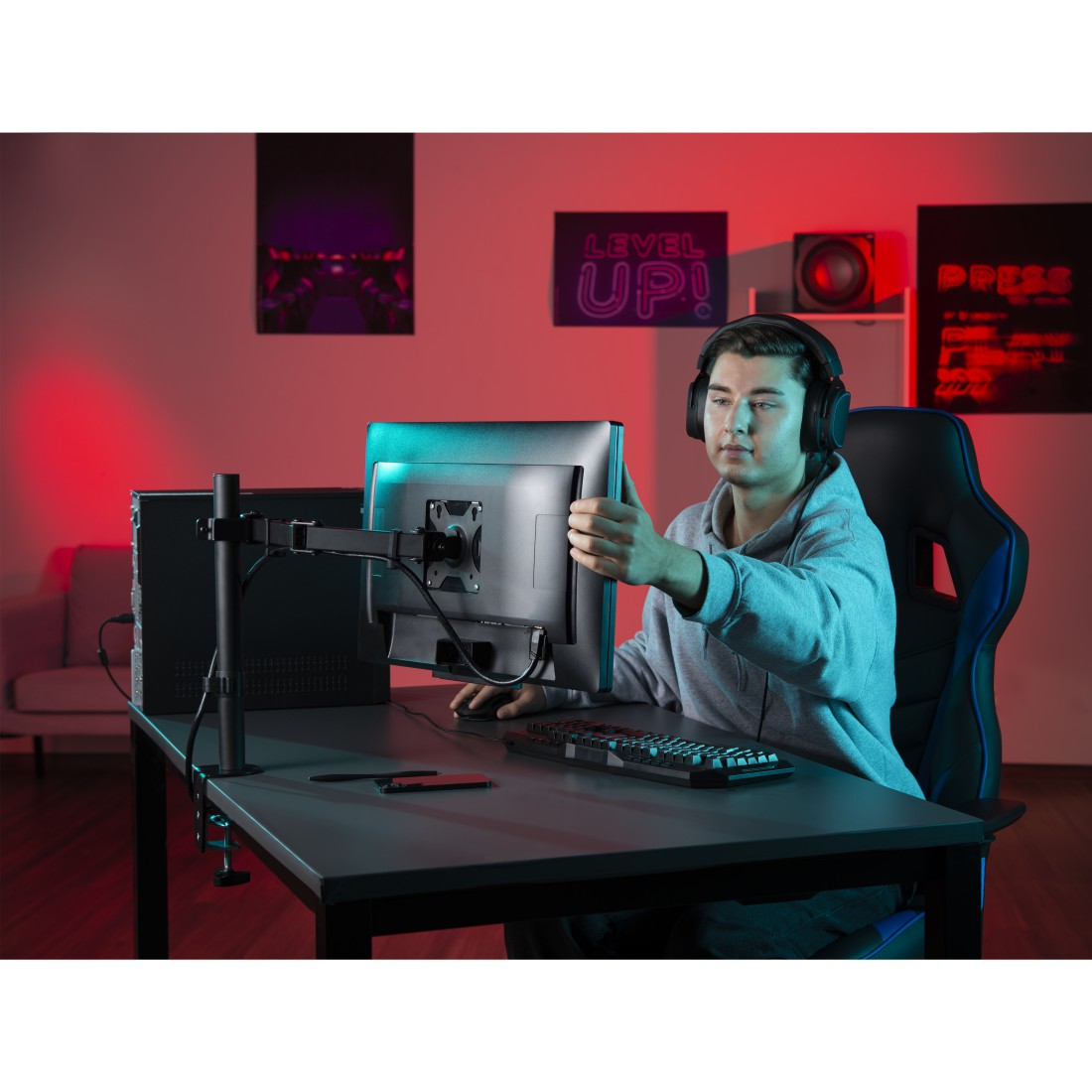 Hombre con auriculares, ajustando monitor, configuración de escritorio, soporte de monitor, teclado, letrero 'Level Up!'.