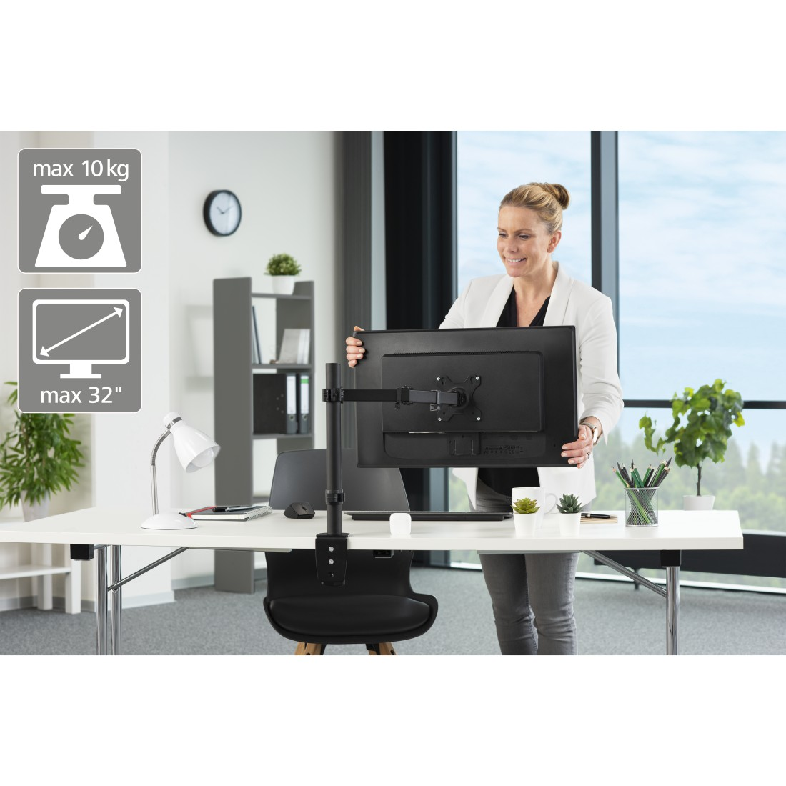 Mujer coloca un monitor negro en un escritorio blanco. Iconos muestran peso y tamaño máximos. El fondo es una oficina.
