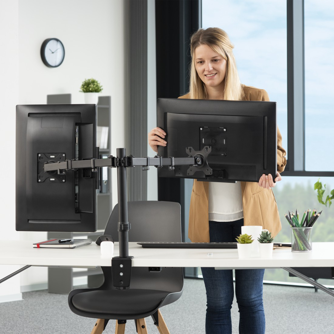 Mujer ajustando monitor, en escritorio con otro monitor.