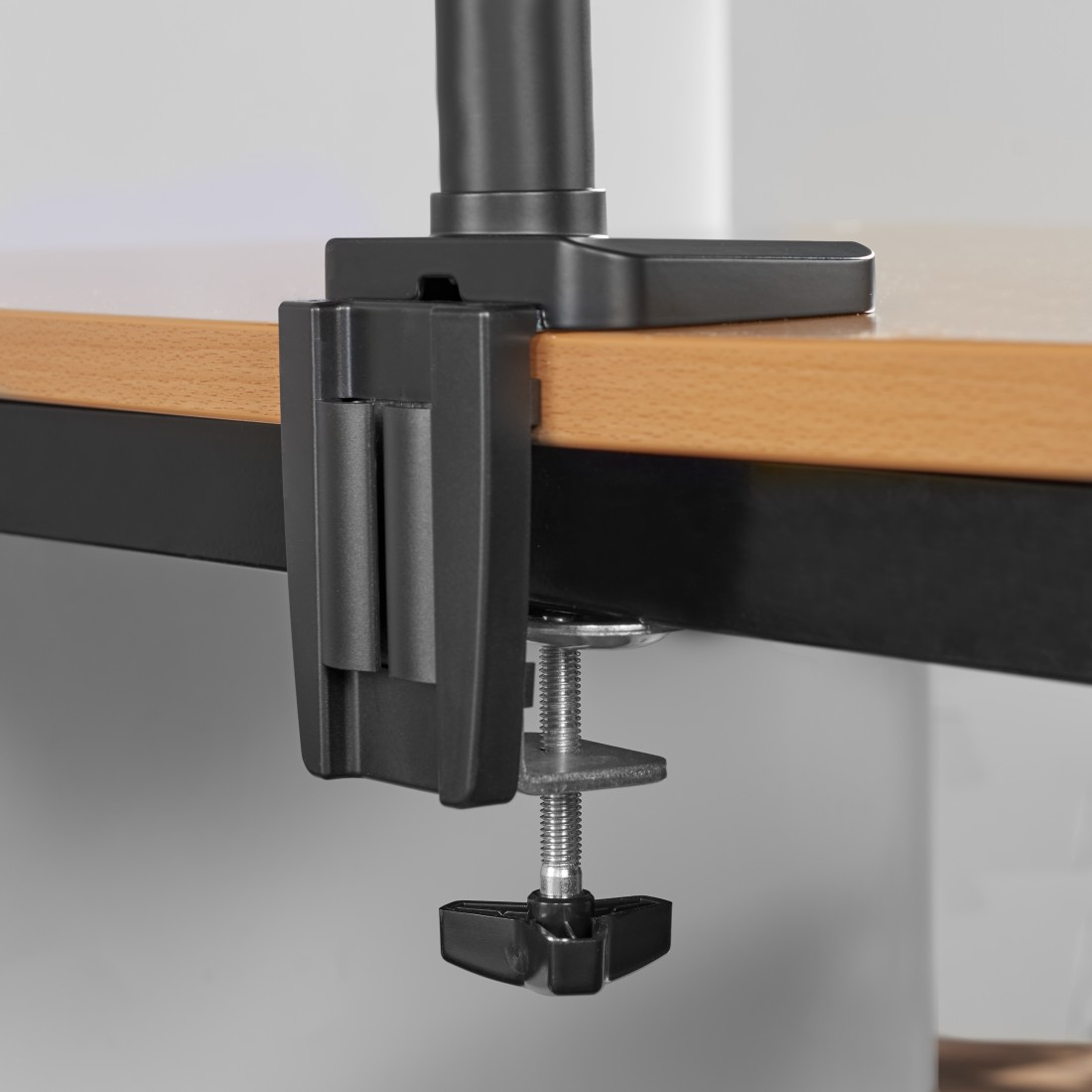 Primer plano de una abrazadera negra para soporte de monitor. Está sujeta a un escritorio de madera.