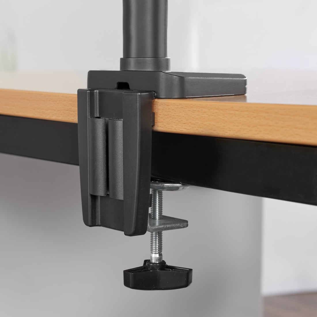 Abrazadera de brazo de monitor negro, montada en mesa de madera con soporte de metal.