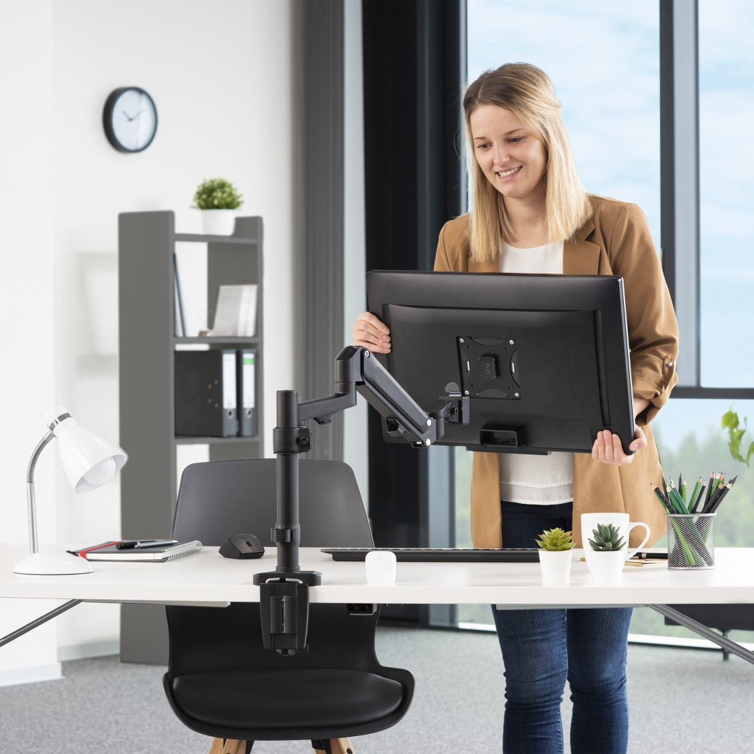 Mujer sosteniendo monitor en un soporte de escritorio negro. Escritorio con superficie blanca.