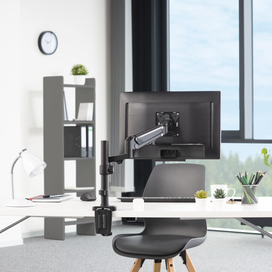 Escritorio de oficina moderno con brazo de monitor. Monitor, lámpara y accesorios son visibles.