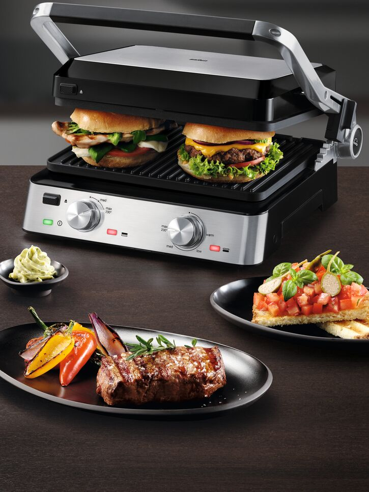 Gegrillte Burger und Steak auf Tellern, mit Beilagen. Dunkler Holztisch.