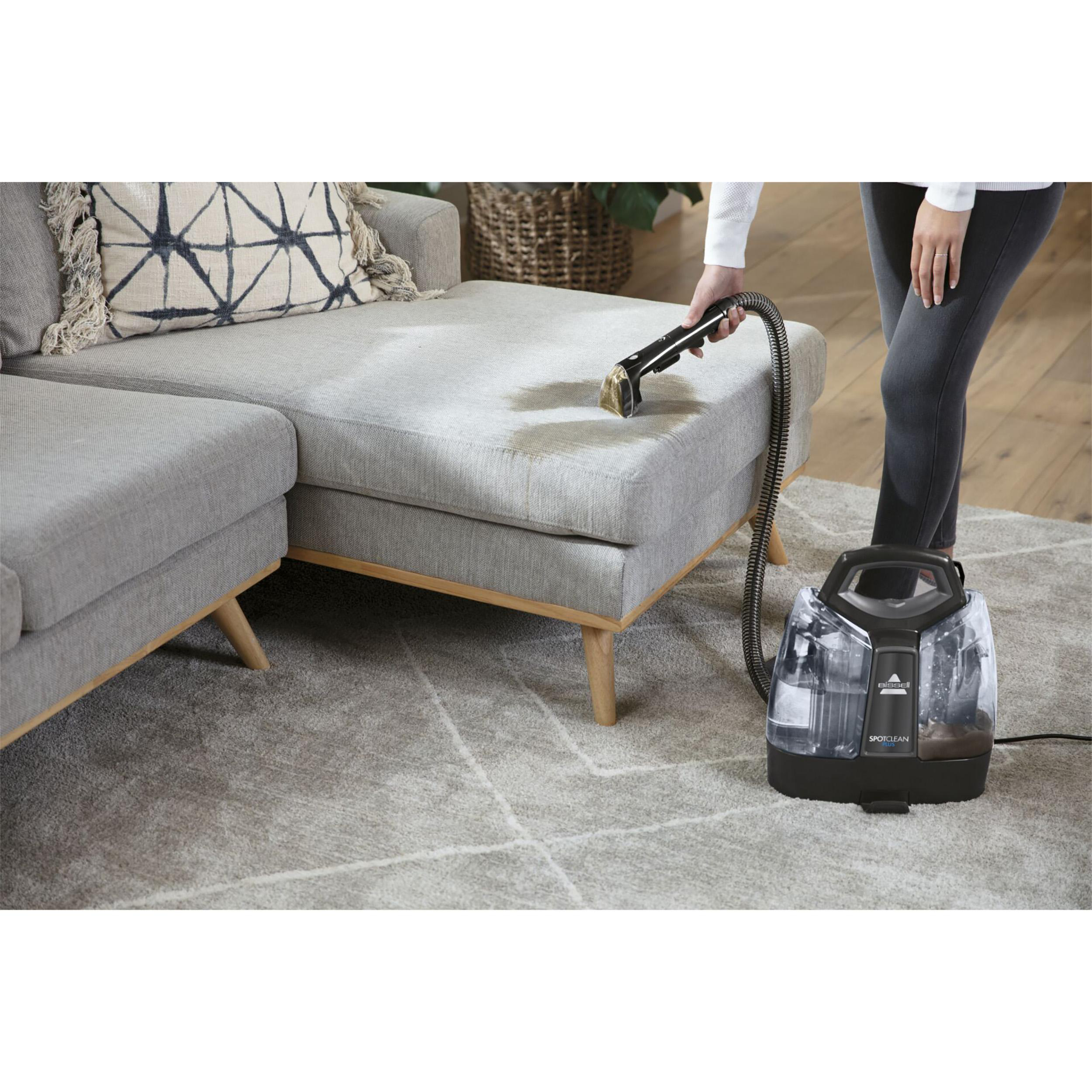 Person reinigt ein Sofa mit einem Fleckenreiniger. Das Sofa ist grau.