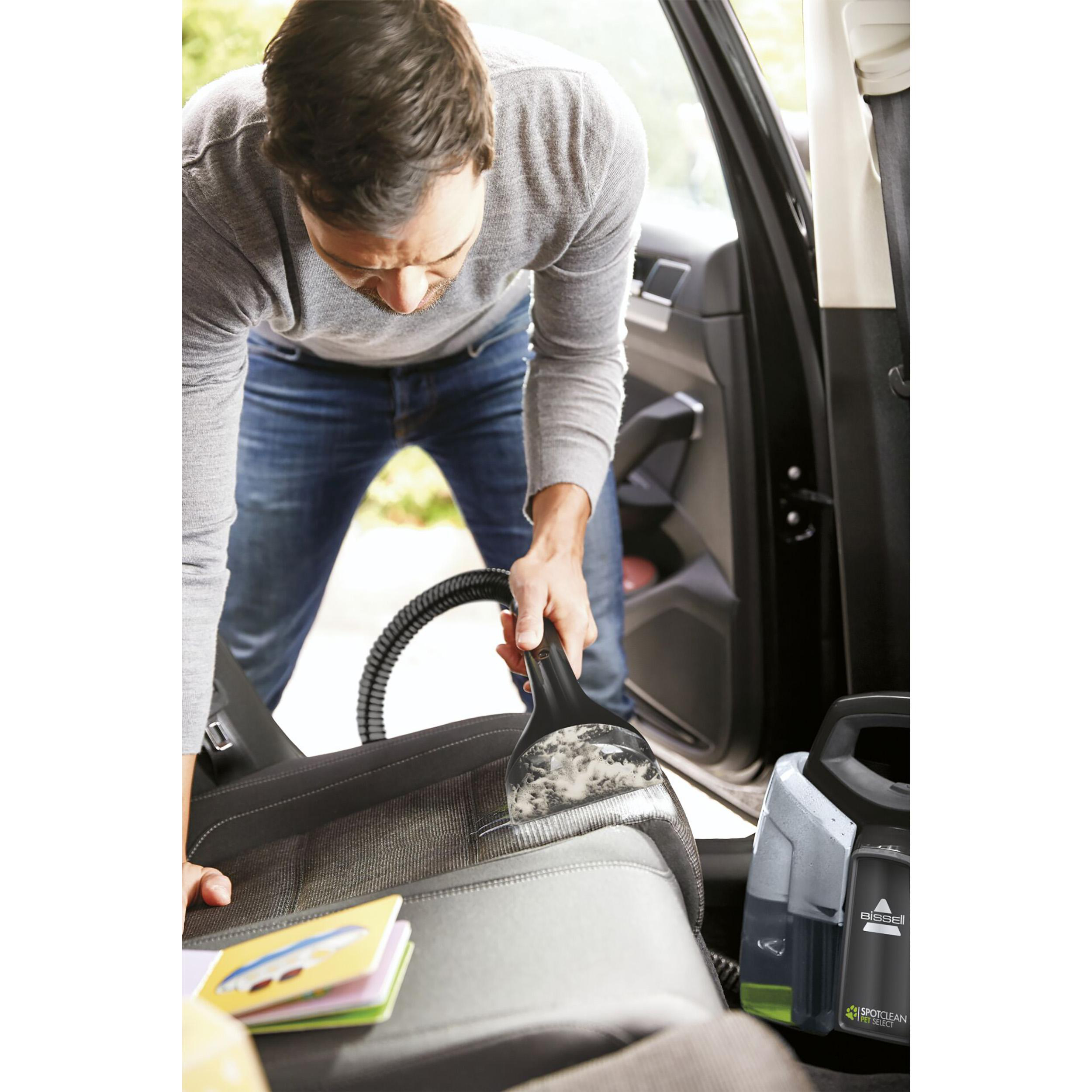 Mann reinigt Autositz mit Bissell SpotClean und Reinigungslösung.