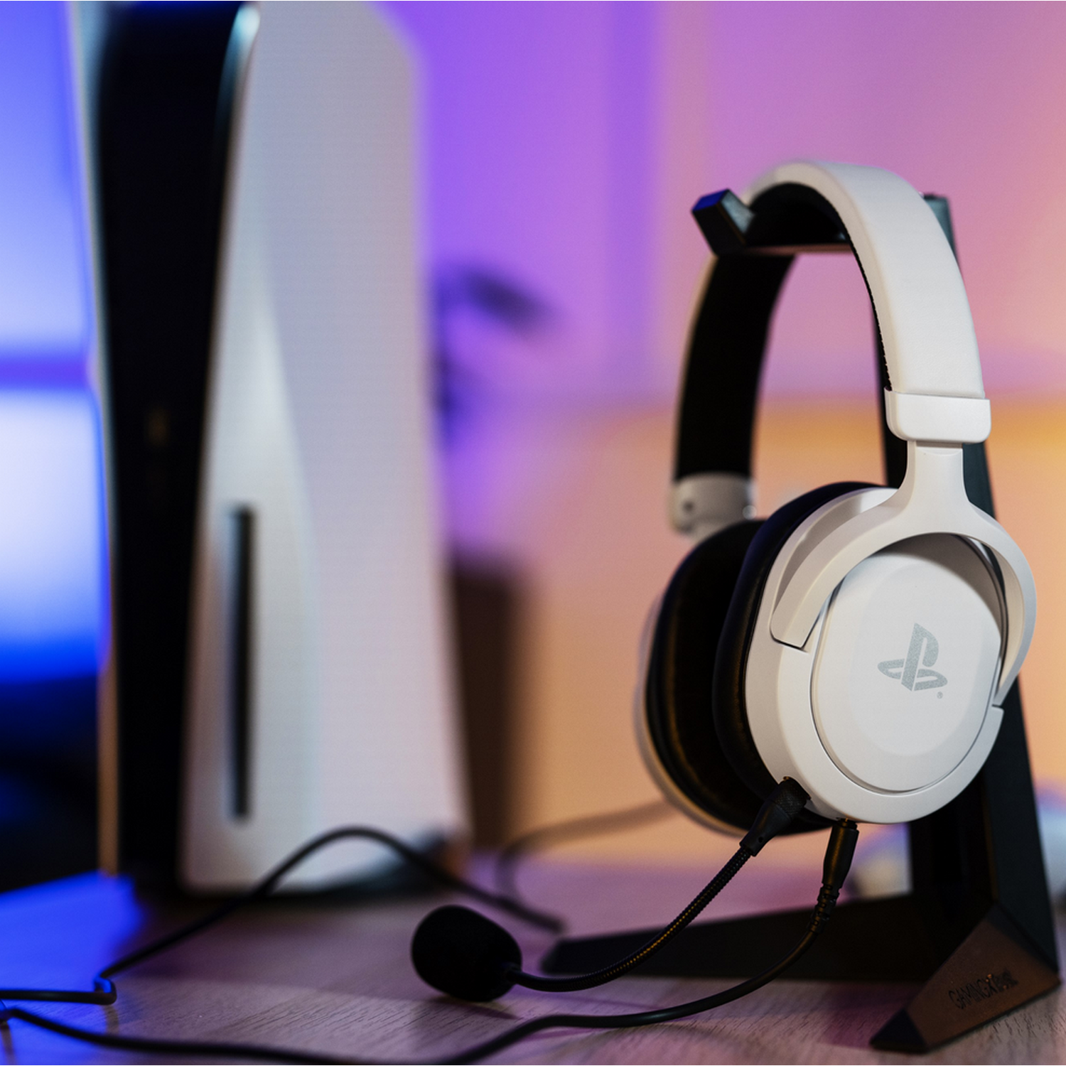 Een witte gamingheadset en een zwarte PS5-standaard, met een PlayStation 5-console op de achtergrond.