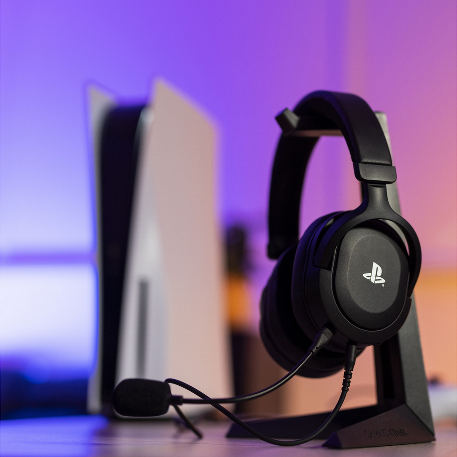 Zwarte gaming headset op een standaard, met een PlayStation 5 op de achtergrond.