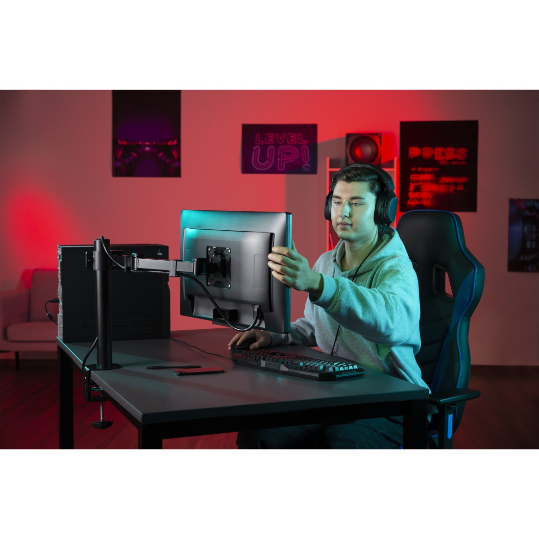 Jugador con auriculares ajustando el monitor, escritorio con teclado, ordenador y silla.