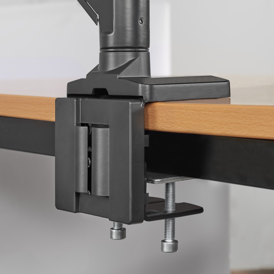 Abrazadera negra de soporte para monitor en un escritorio de madera. Vista de cerca.