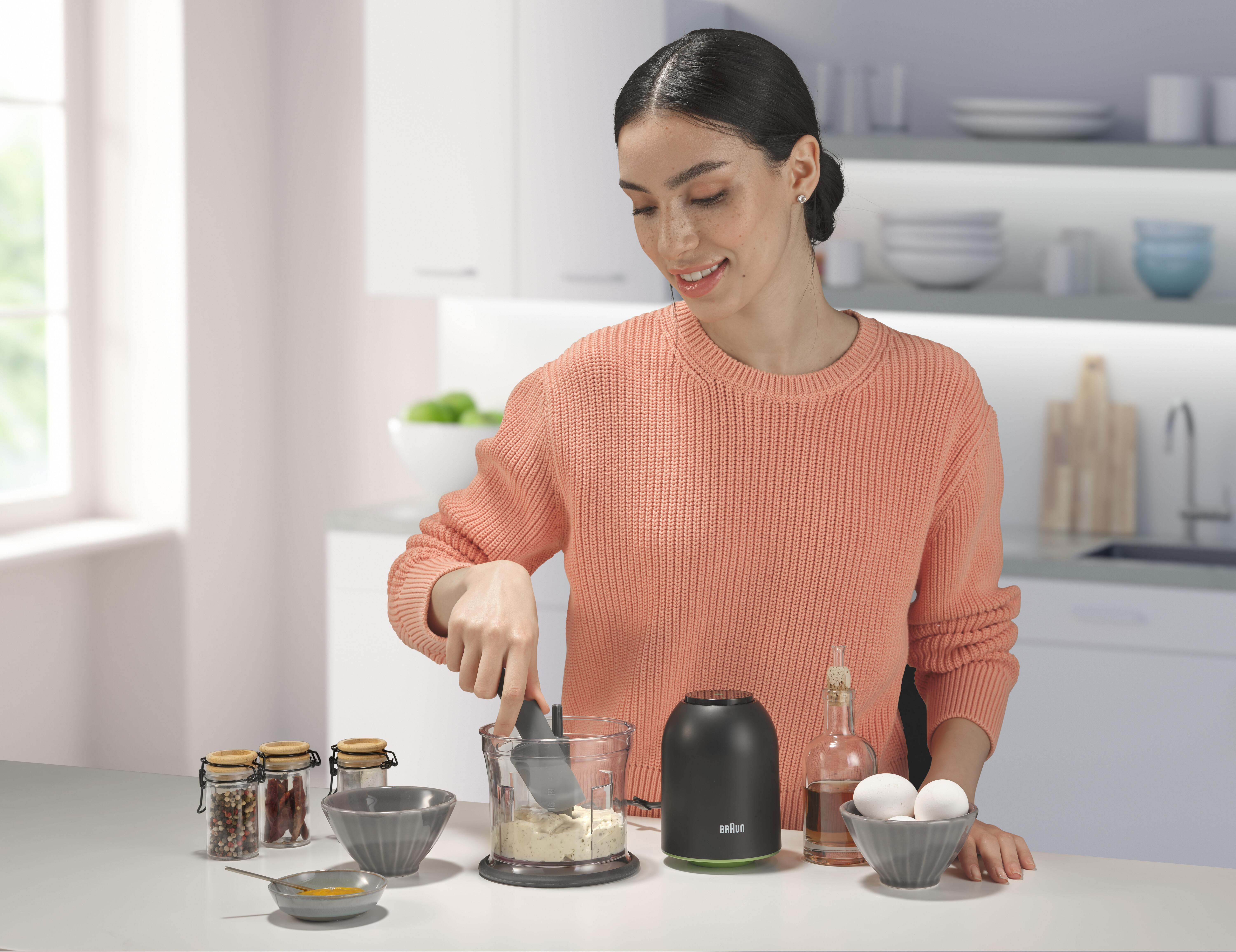 Frau in orangefarbenem Pullover, die einen Foodprozessor mit Lebensmitteln benutzt.