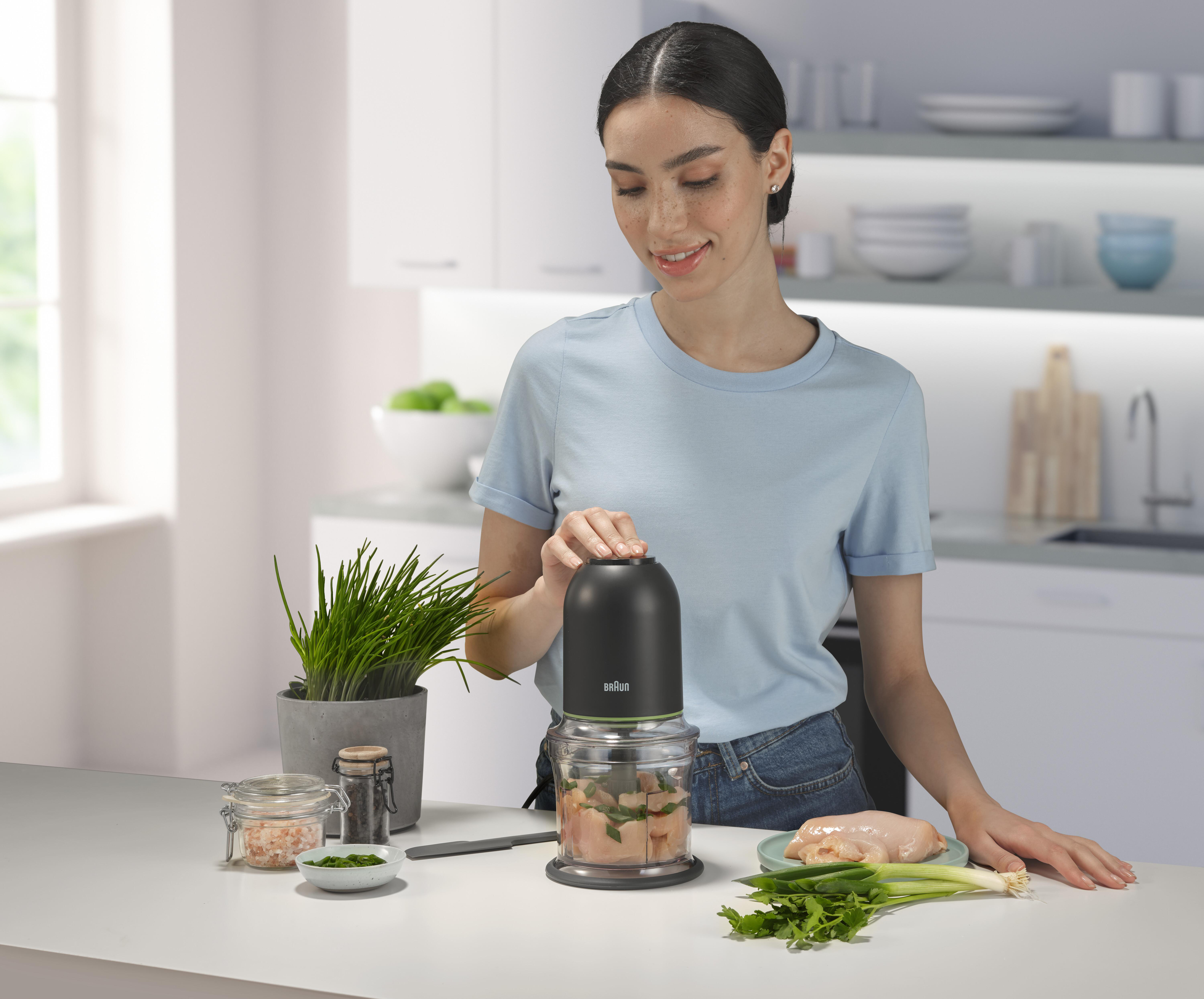 Eine Frau benutzt einen schwarz-grünen Foodprocessor neben Zutaten auf einer Küchentheke.