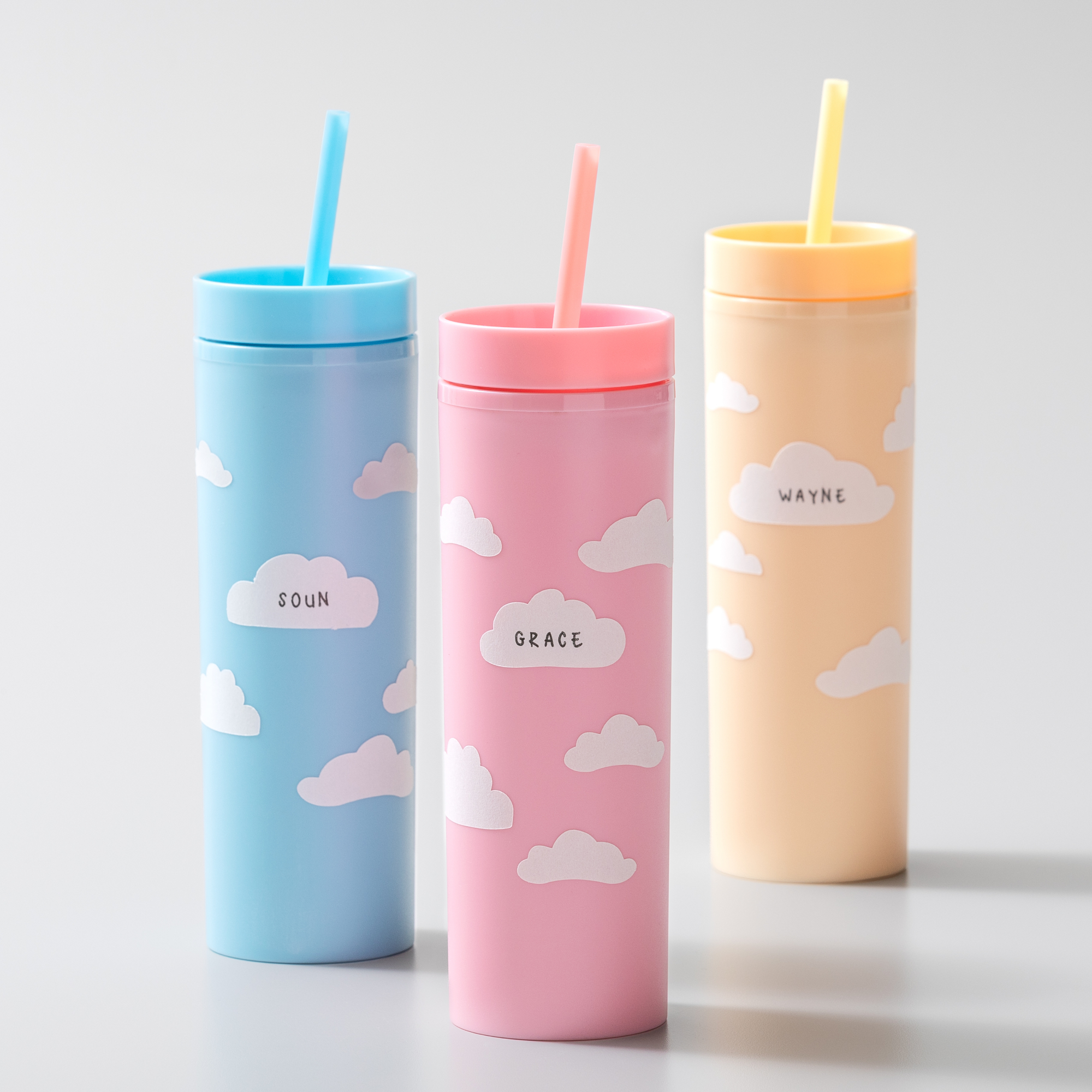 Drei bunte Becher mit Strohhalmen, jeder mit einem Wolkenaufkleber und einem Namen: Soun, Grace und Wayne.