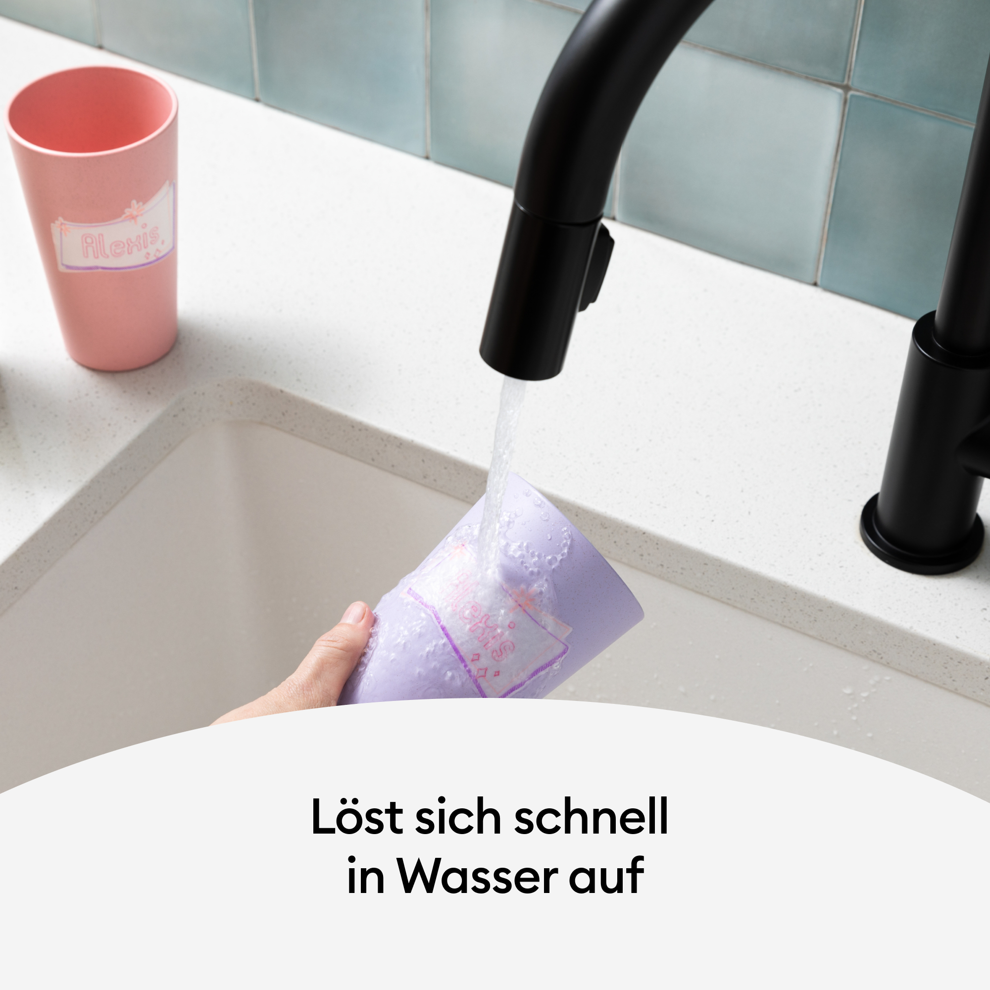 Eine Hand hält einen lila Aufkleber unter fließendem Wasser. Eine rosa Tasse mit „Alex“-Etikett ist sichtbar.