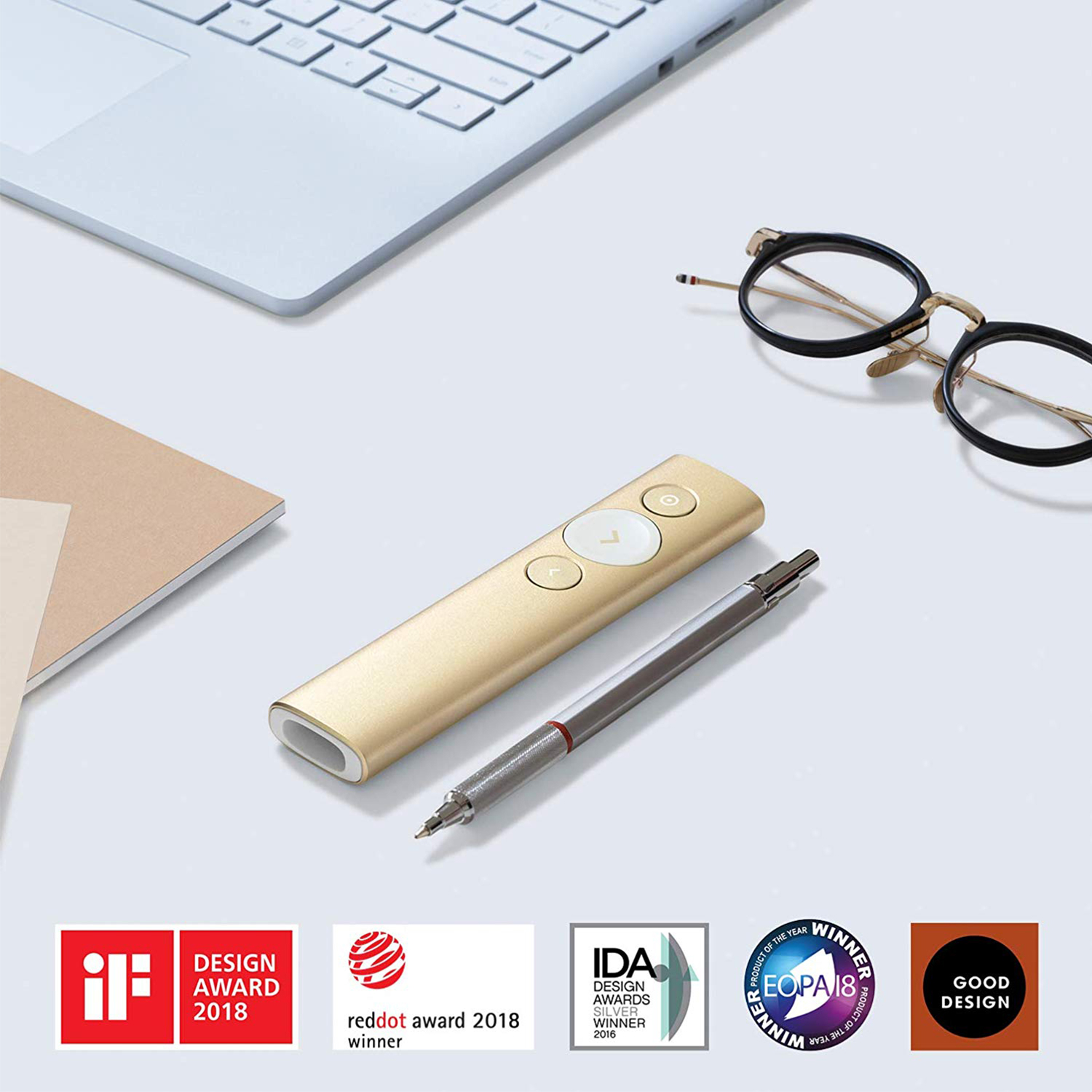 Goldene Fernbedienung, Bleistift, Brille und Auszeichnungen auf weißer Oberfläche, Laptop im Hintergrund.