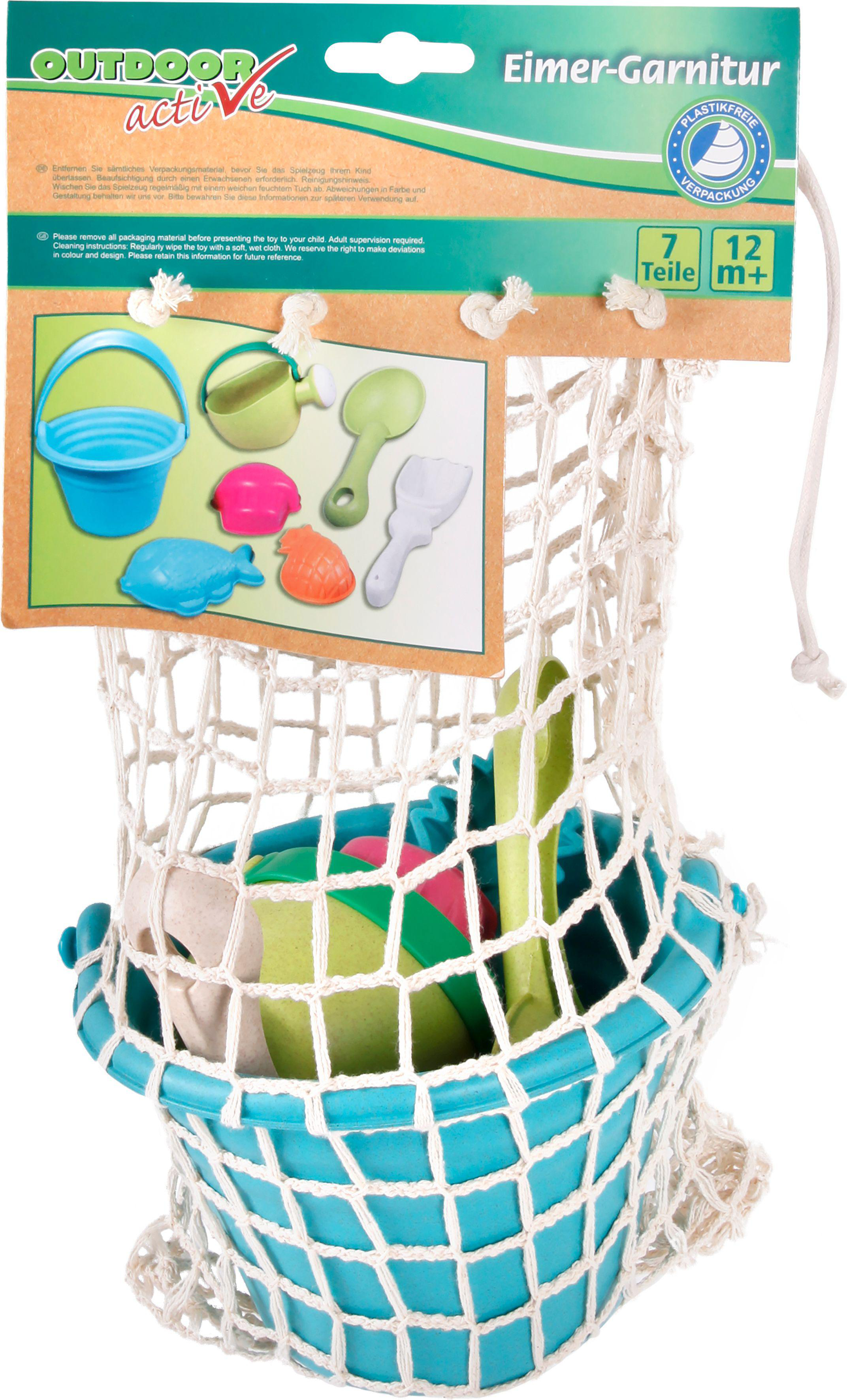 Ein blauer Eimer mit Strandspielzeug in einem weißen Netzbeutel. Das Etikett hat bunte Spielzeugbilder.