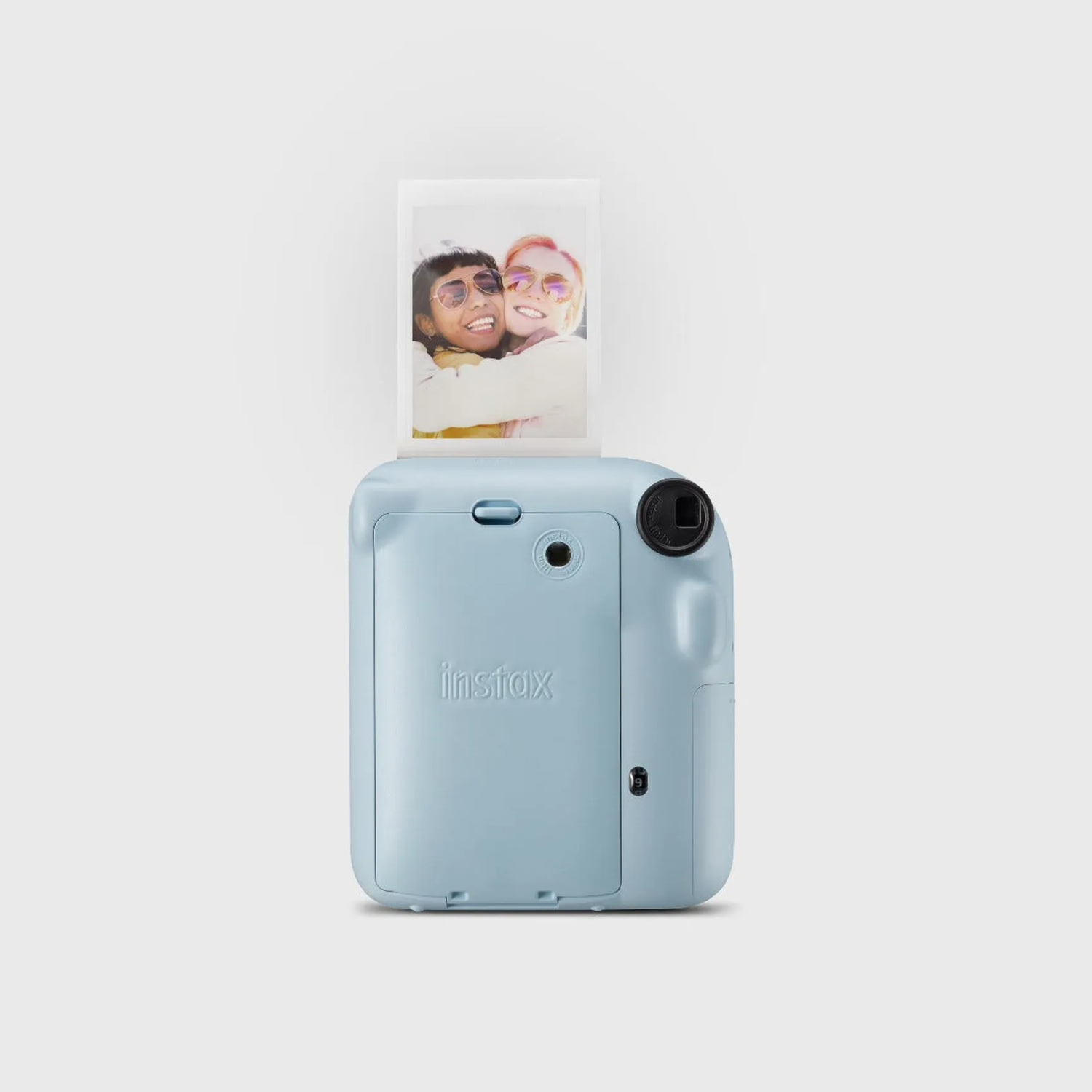 Un appareil photo Instax bleu clair avec une impression photo qui sort, montrant deux femmes souriantes.