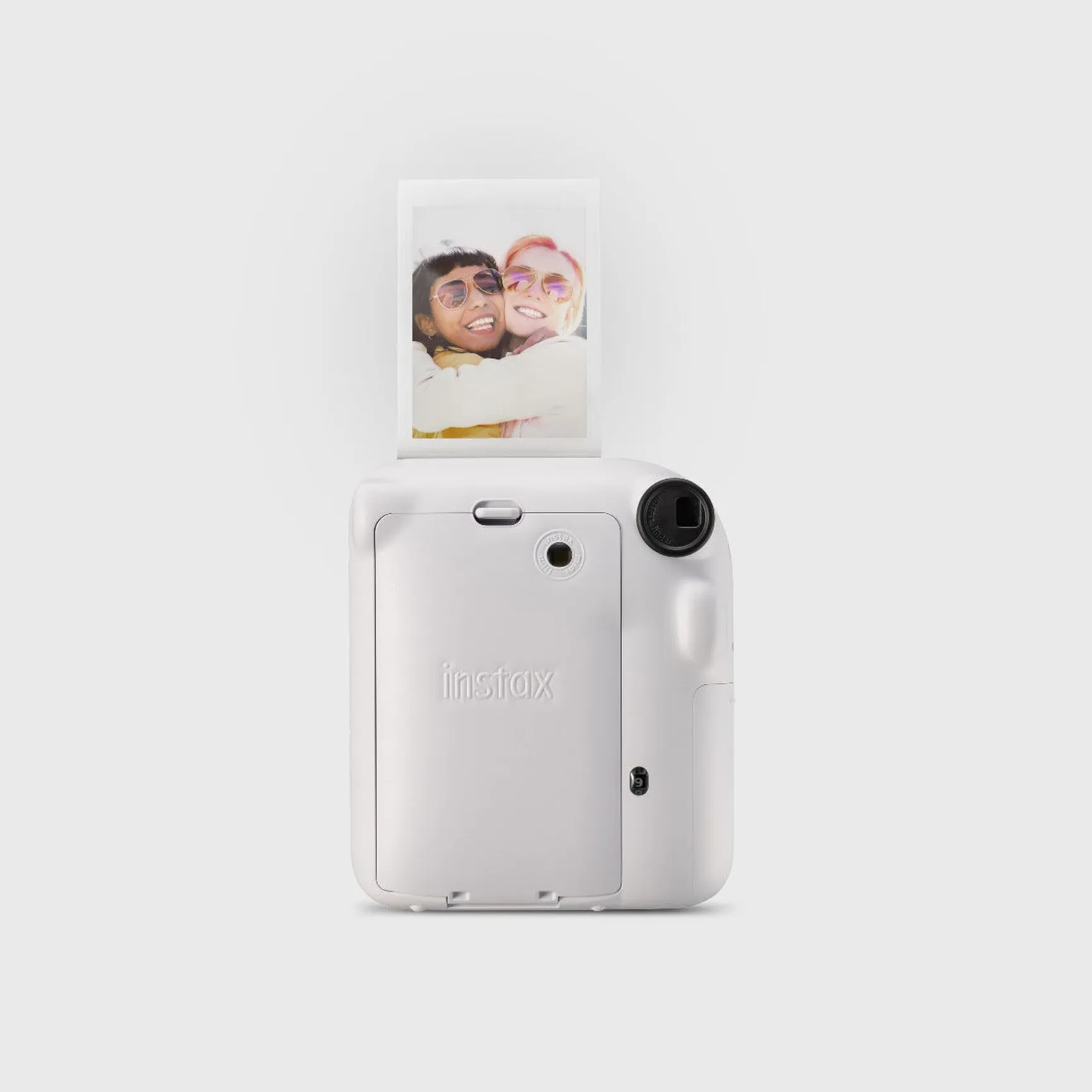 A white Instax camera with a photo coming out, showing two smiling women.