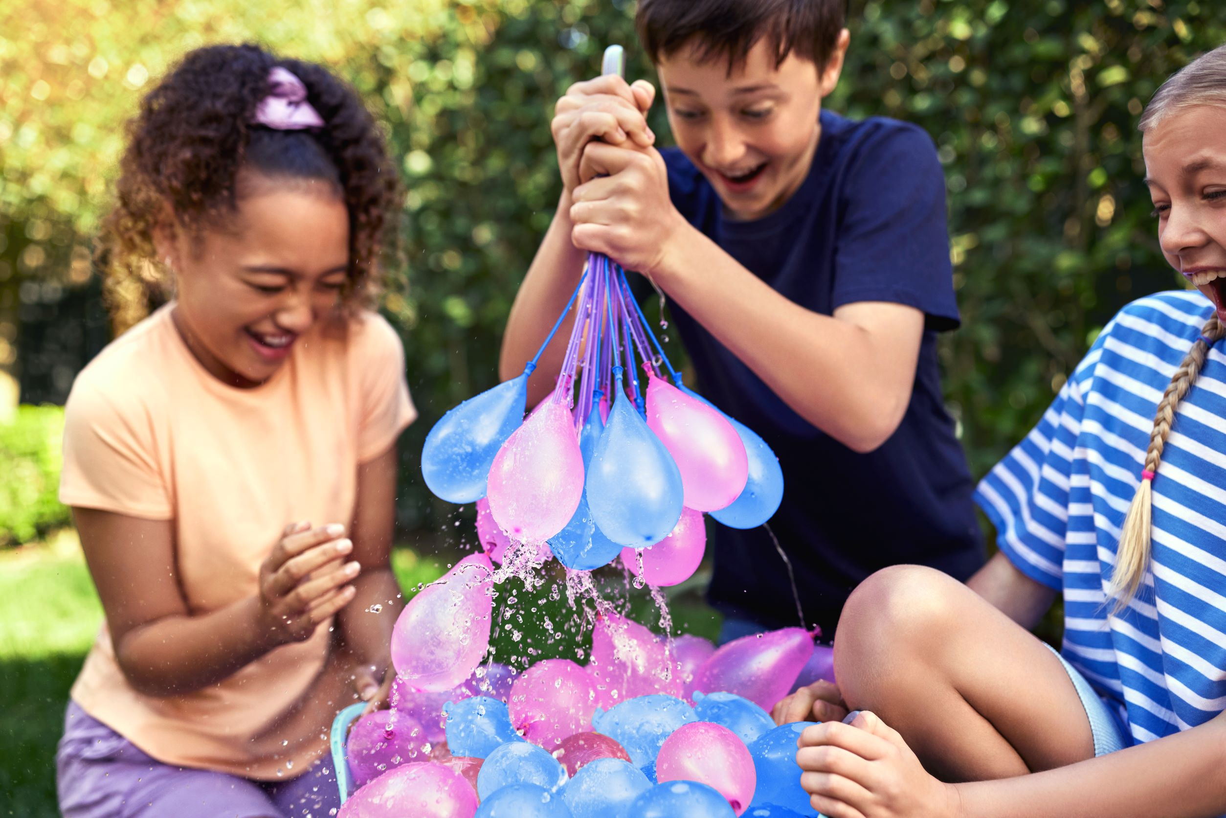Kinder spielen im Garten mit Wasserbomben.